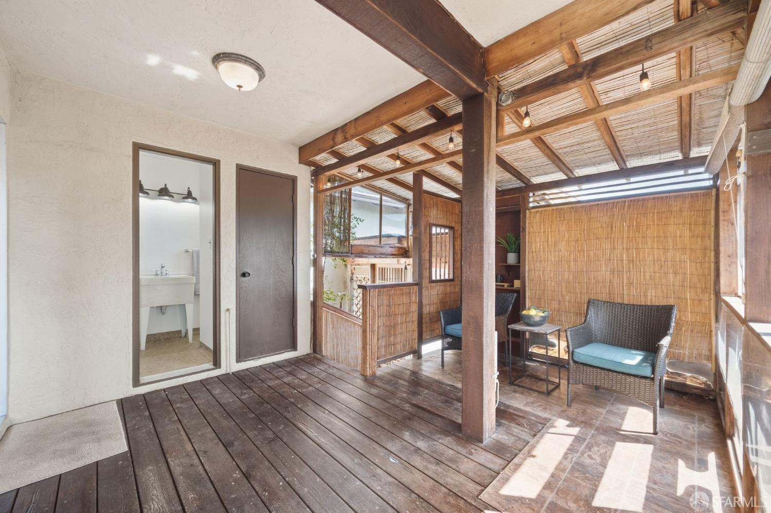 Covered patio with exposed timber beams, bamboo screens, and wicker seating on a wood deck.