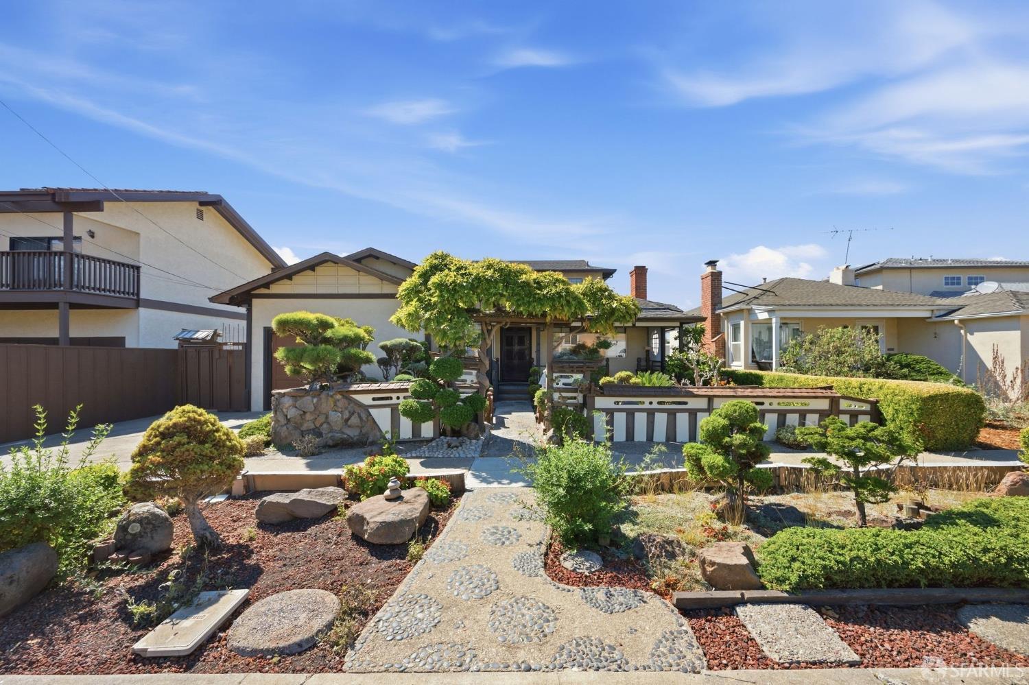 Home front with a pebble path, leafy pergola, and sculpted garden shrubs.