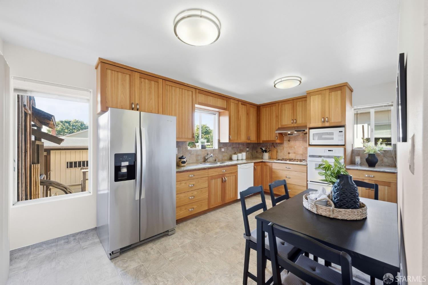 Kitchen with honey-toned wood cabinets, stainless steel appliances, and a black dining table.