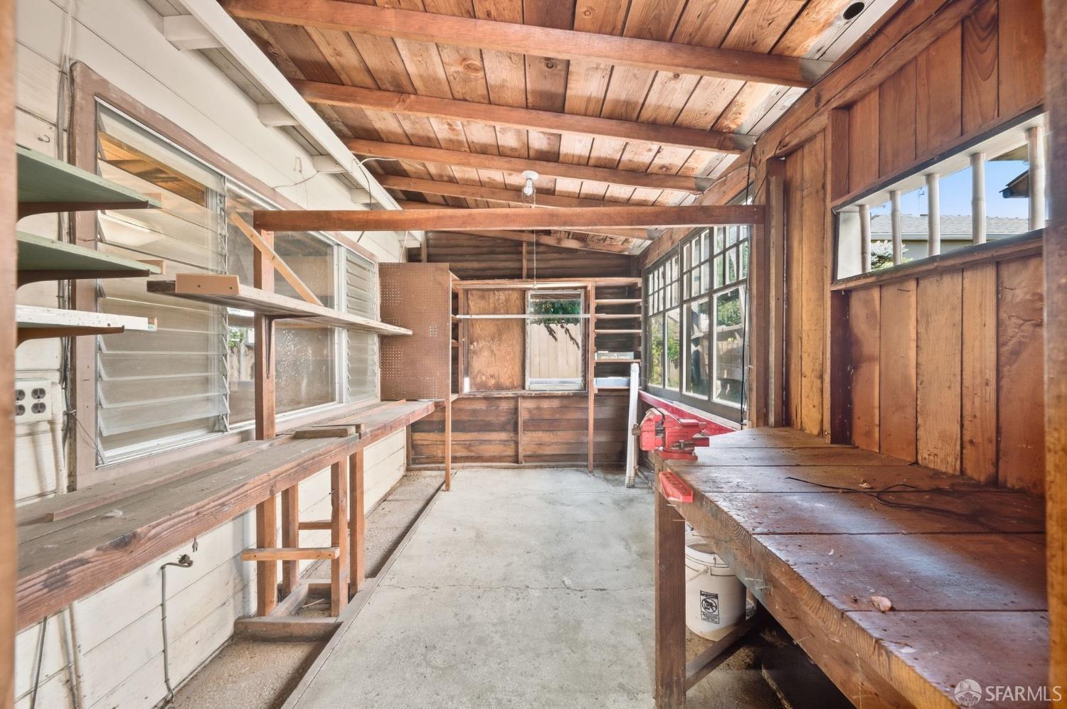 Wooden workshop interior with built-in workbenches, shelving, windows, and a concrete floor.