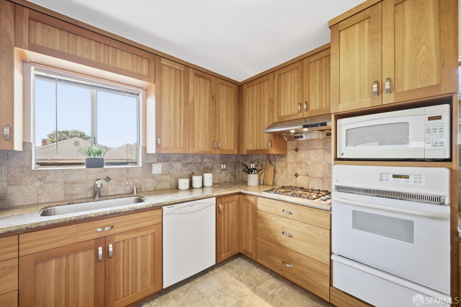 Kitchen with warm wood cabinets, tiled backsplash, and a window above the sink.