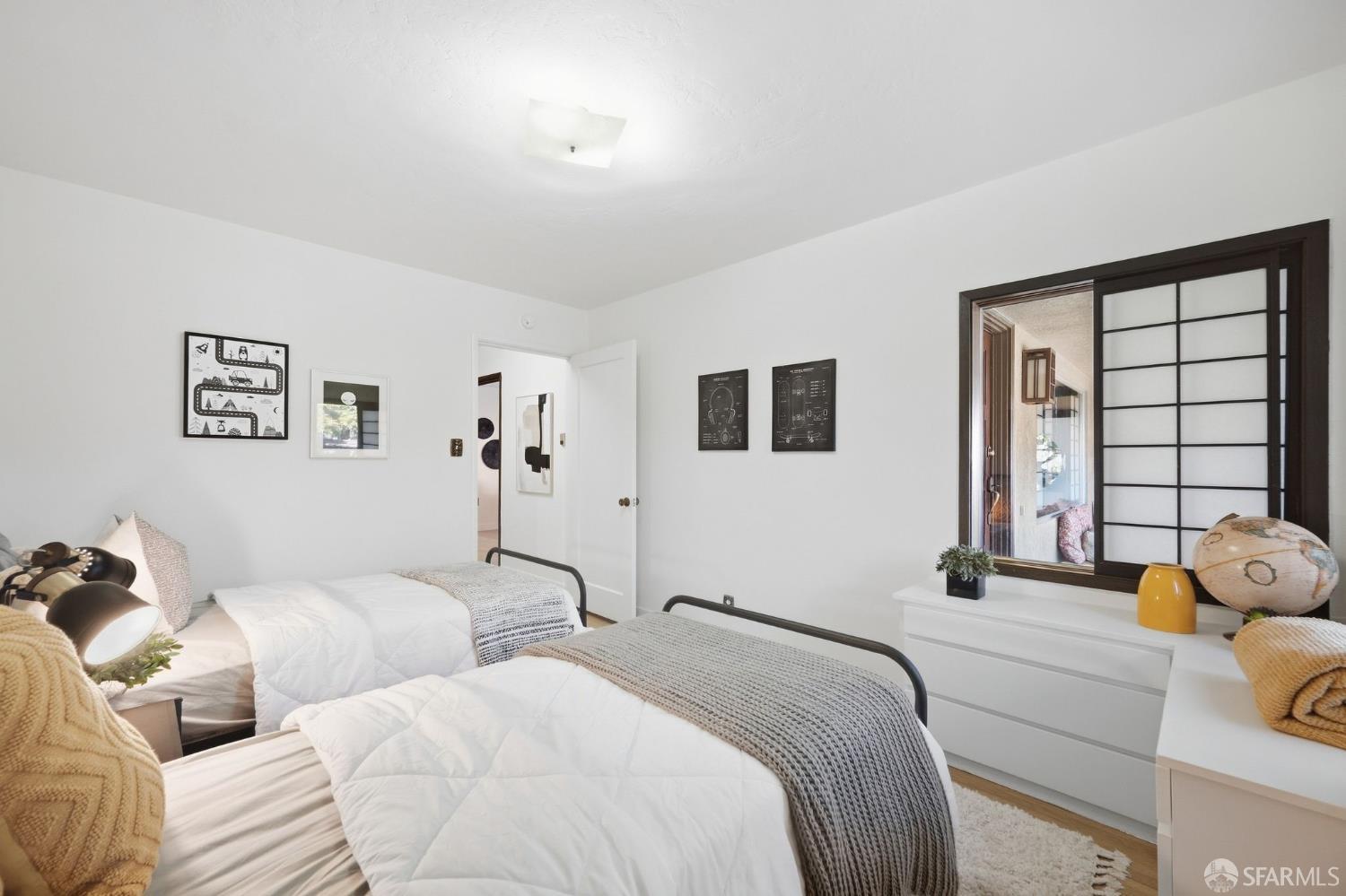 Bedroom with two white beds, gray knit throws, and a dark-framed interior window.