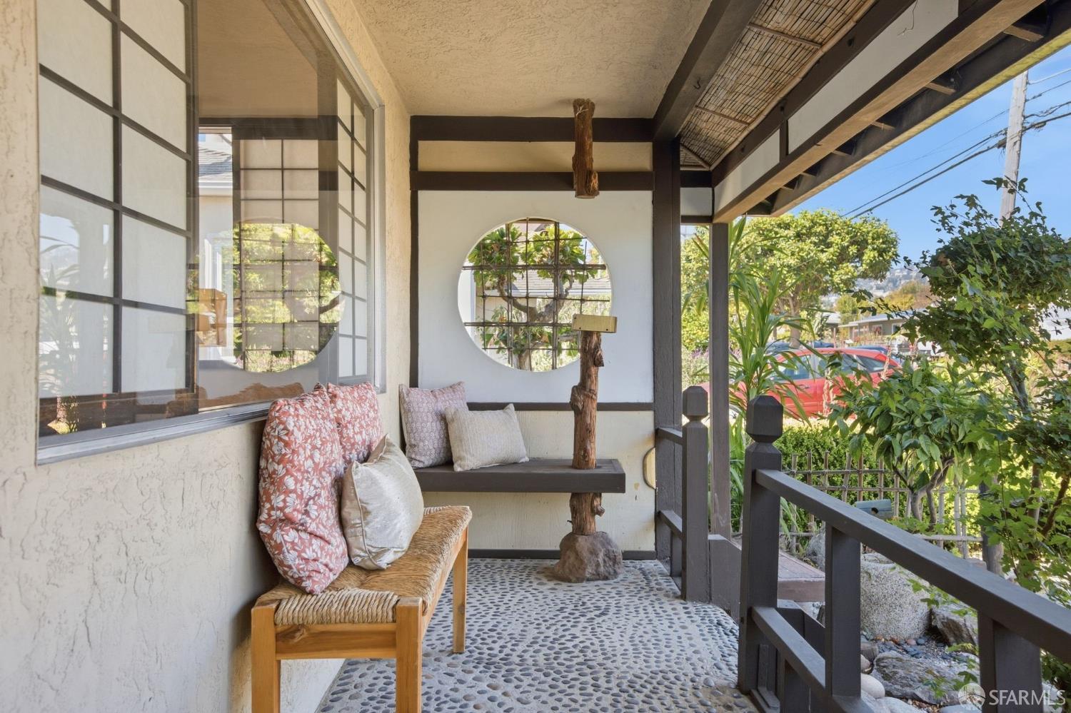 Covered porch with a circular window, pebble-stone floor, and cushioned wooden seating.