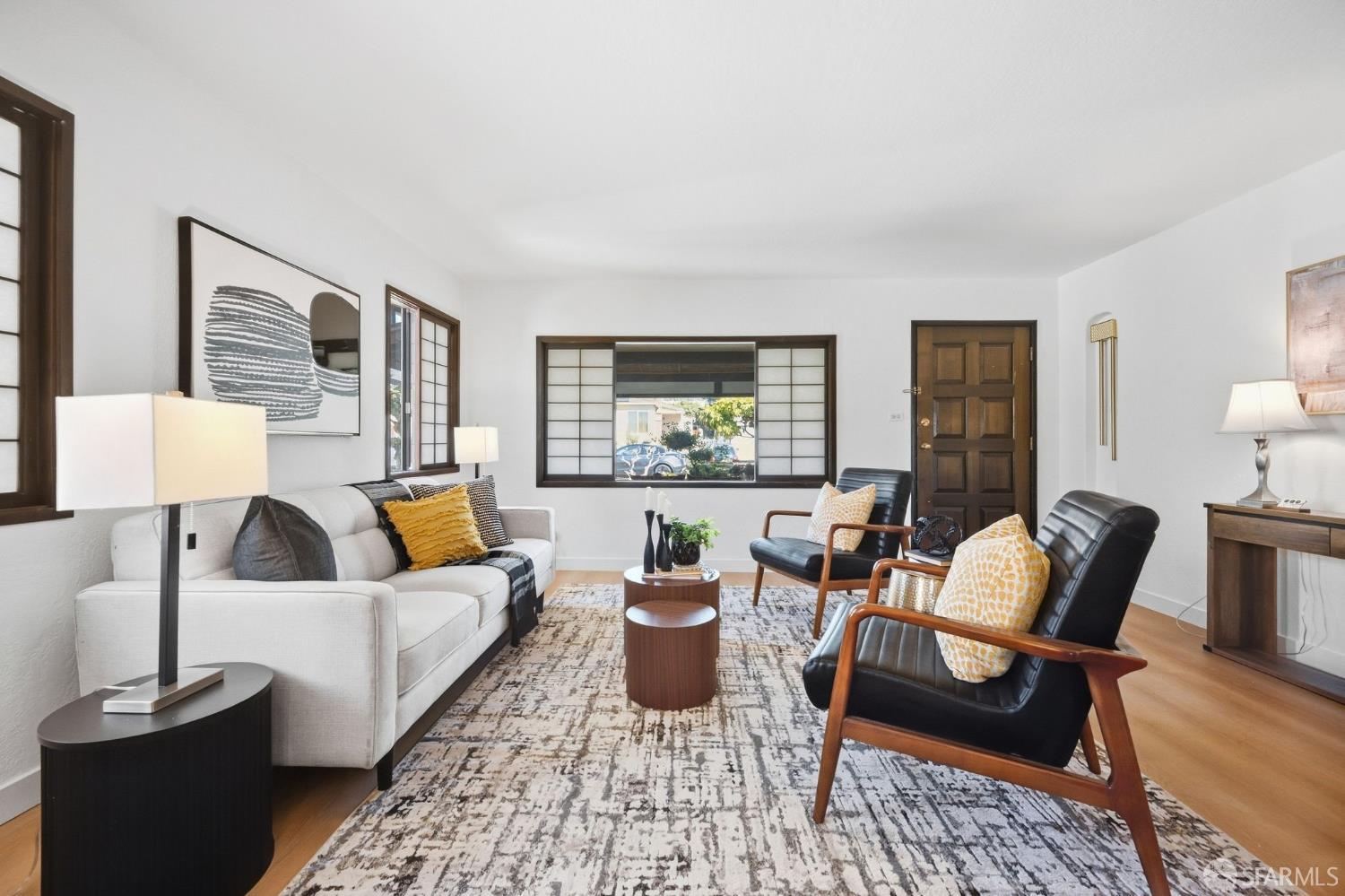 Living room with a white sofa, black leather lounge chairs, and wood-trimmed windows.