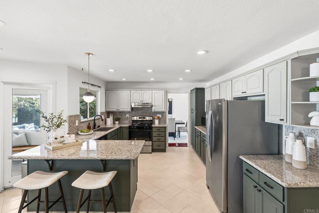 Kitchen with a granite island, dark green cabinets, and stainless steel appliances.
