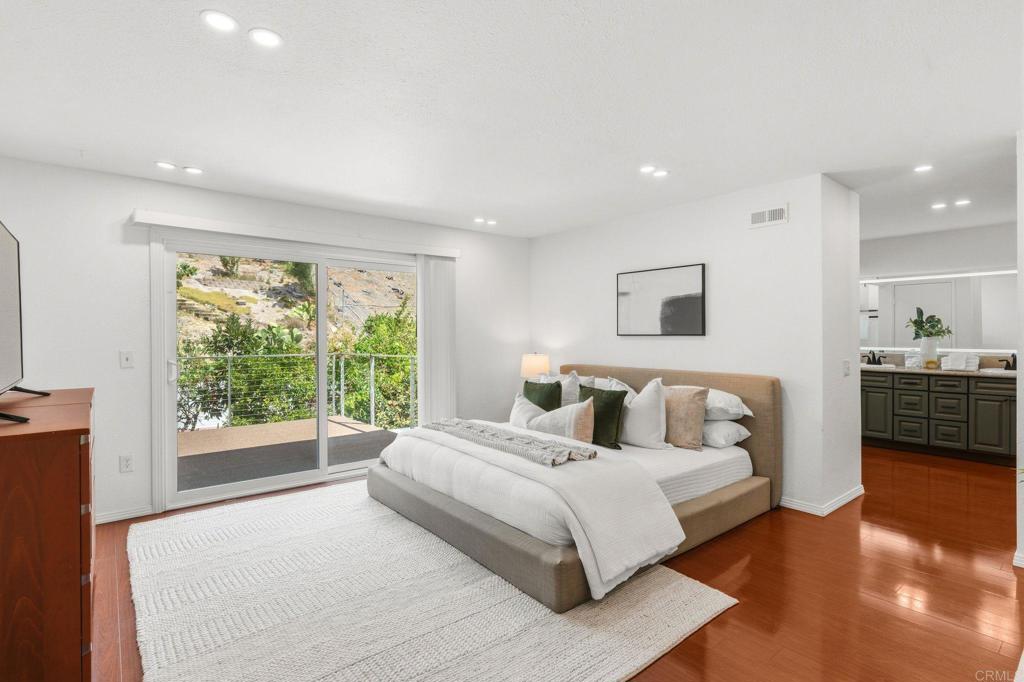 Staged bedroom with sliding glass doors opening onto a patio overlooking greenery and a rocky slope.