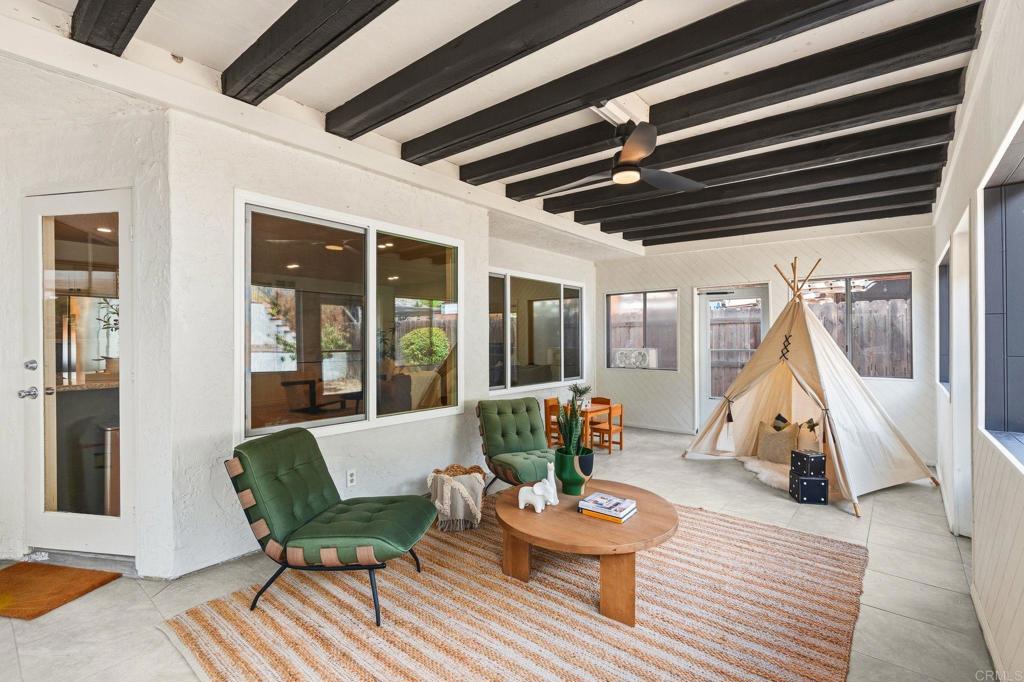 Enclosed patio with dark ceiling beams, green lounge chairs, and a teepee beside large windows.