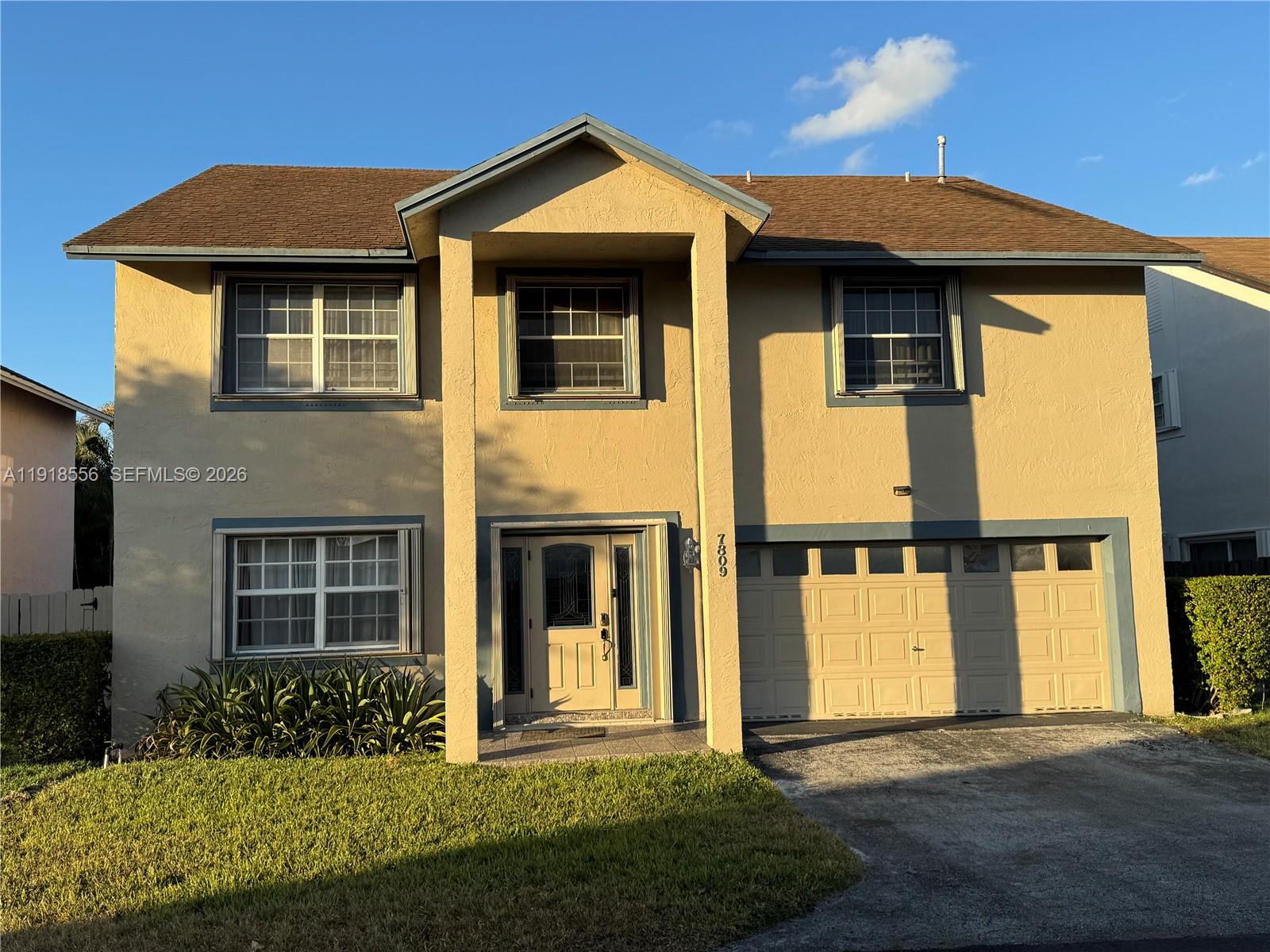 Two-story yellow stucco house with a covered entrance and attached garage in warm evening sunlight.