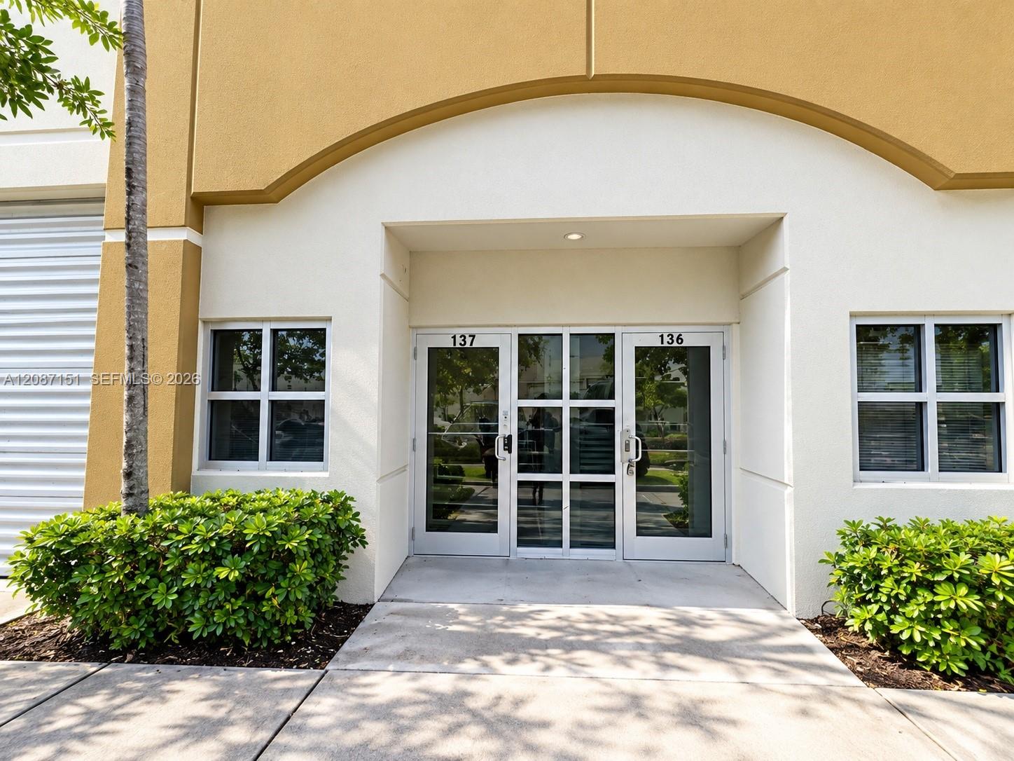 Building entrance with glass doors numbered 137 and 136, framed by shrubs.