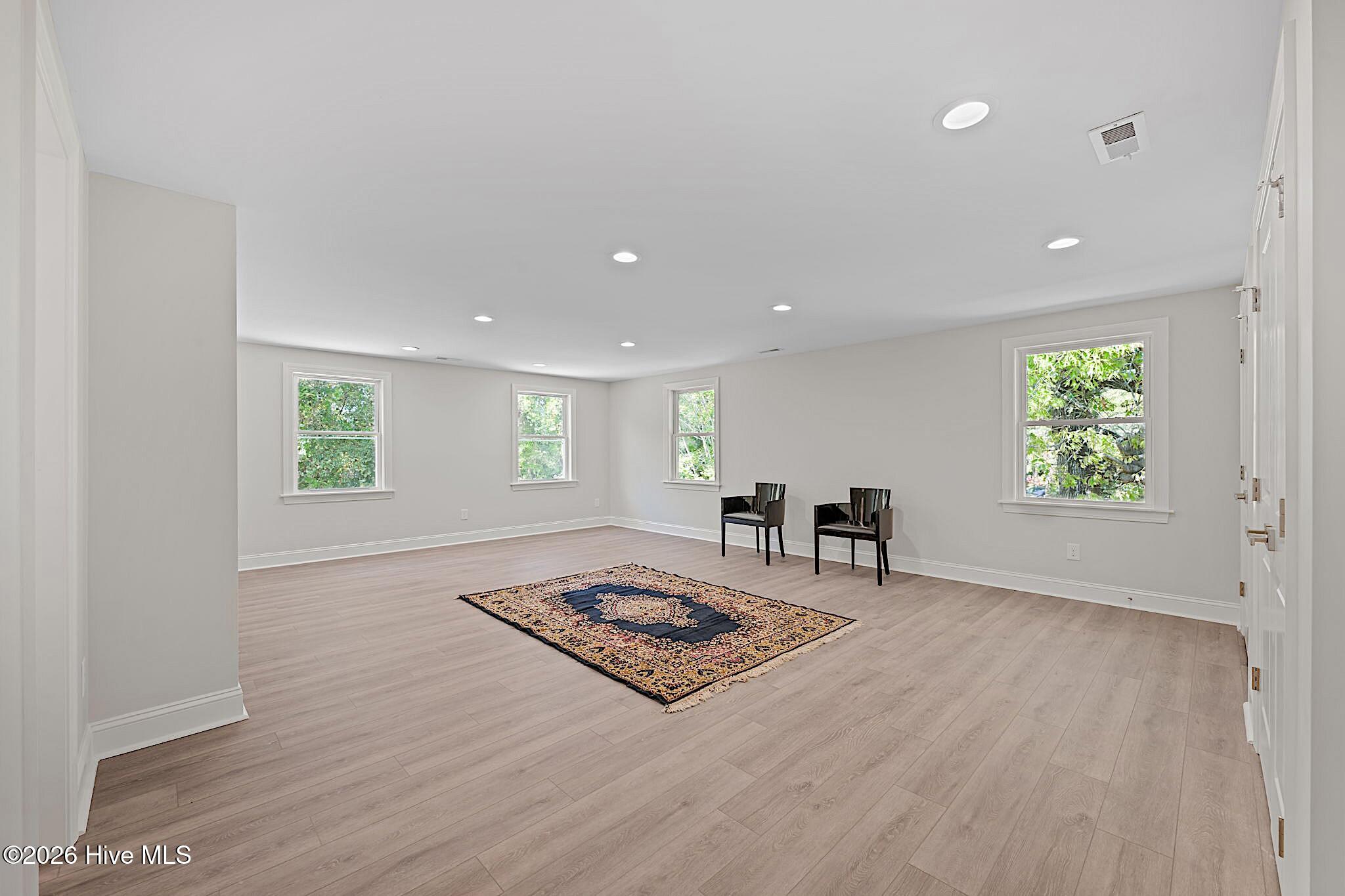 Spacious living room with light flooring, four windows, two chairs, and a patterned rug.
