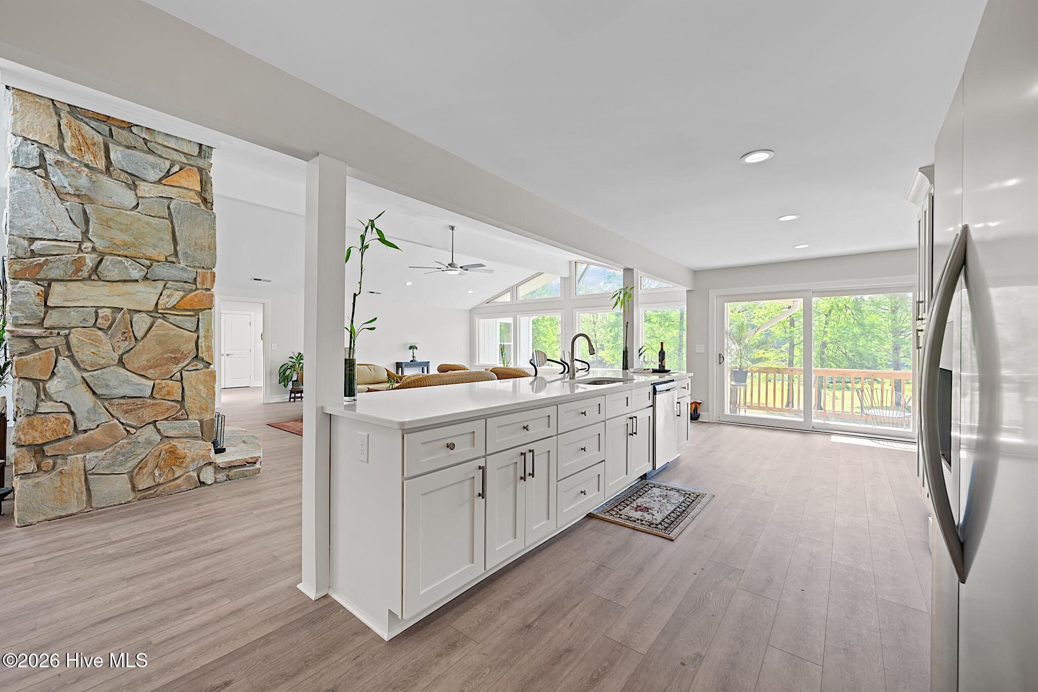 Open-plan kitchen with a long white island, stone fireplace wall, and glass doors to a deck.