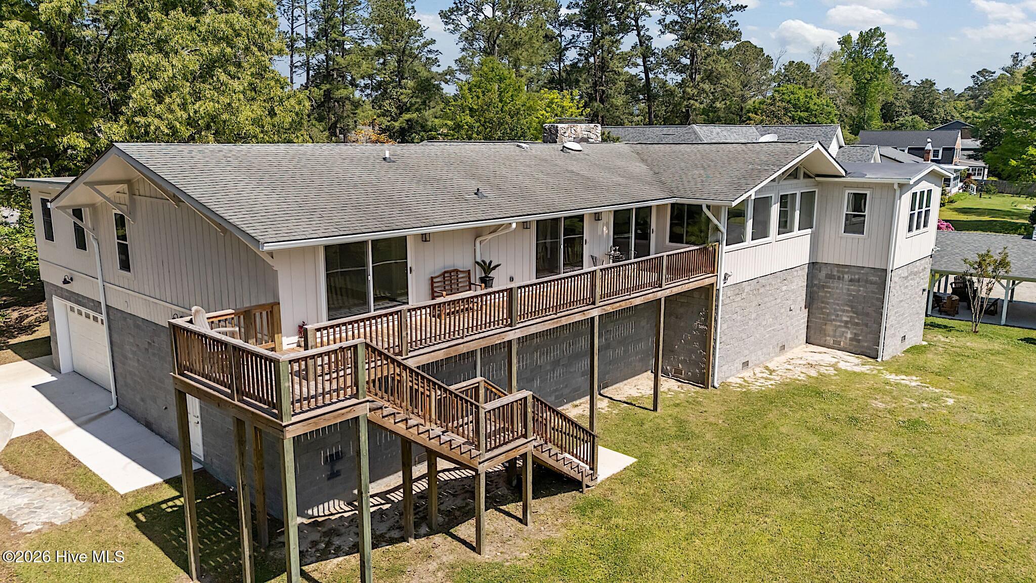 Rear of a light-colored home with a long raised deck and exterior stairs