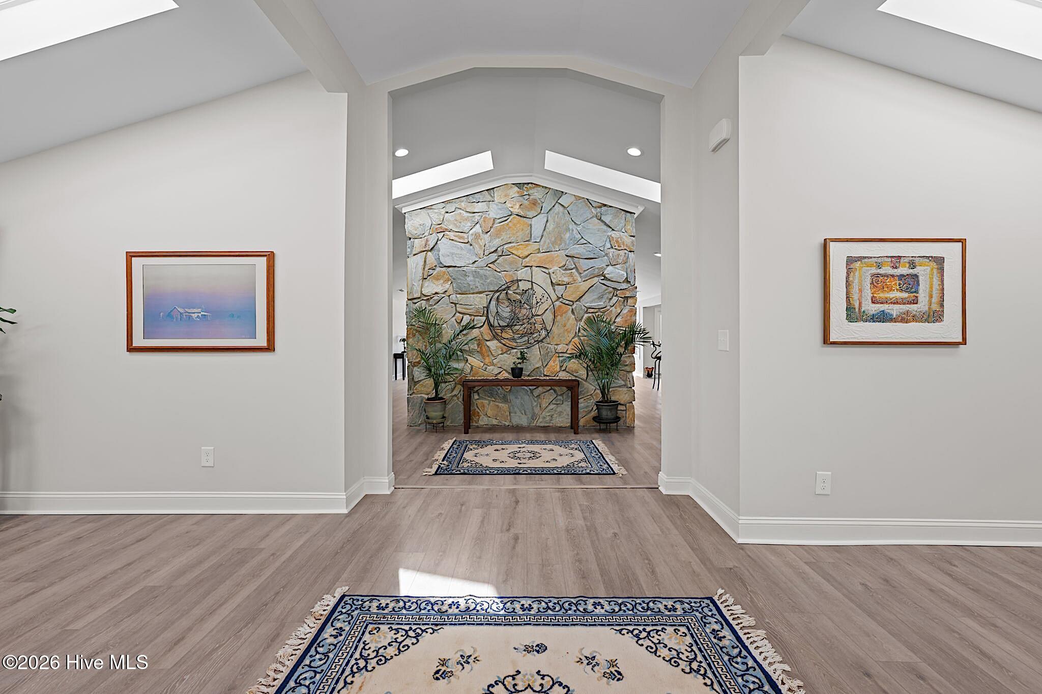 Entry hall with a vaulted ceiling, tall stone accent wall, wood-look flooring, and patterned rugs.