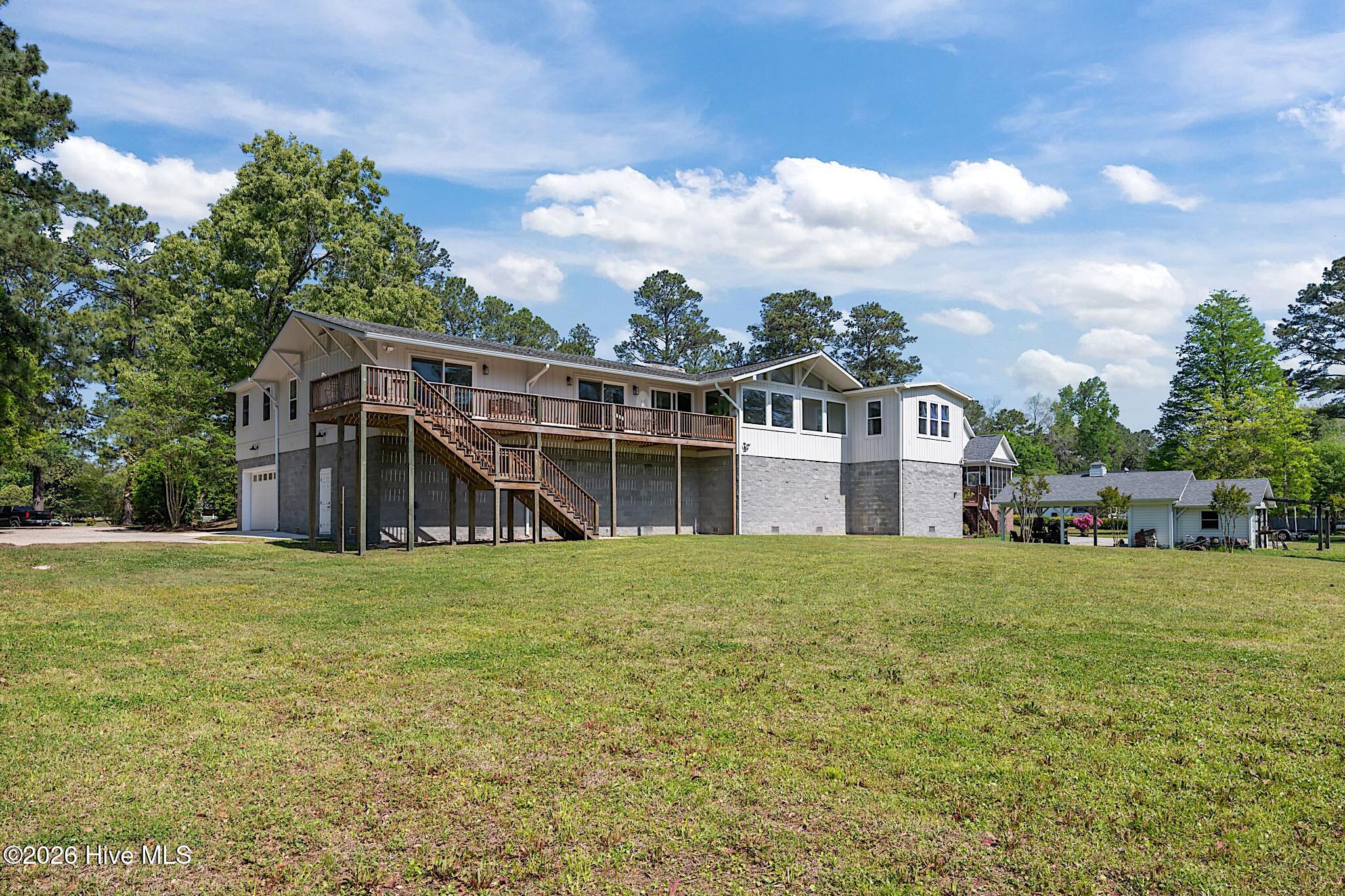 Raised white house with a long wooden deck and staircase overlooking a broad grassy lawn.