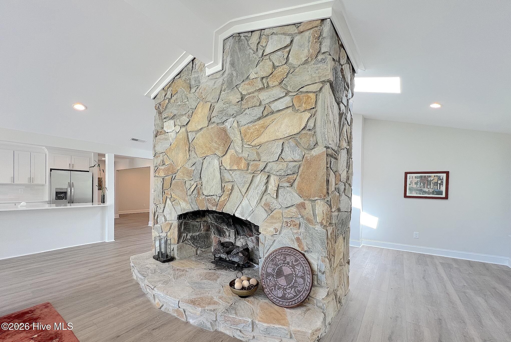 Living area with a tall stone fireplace and open kitchen to the left.
