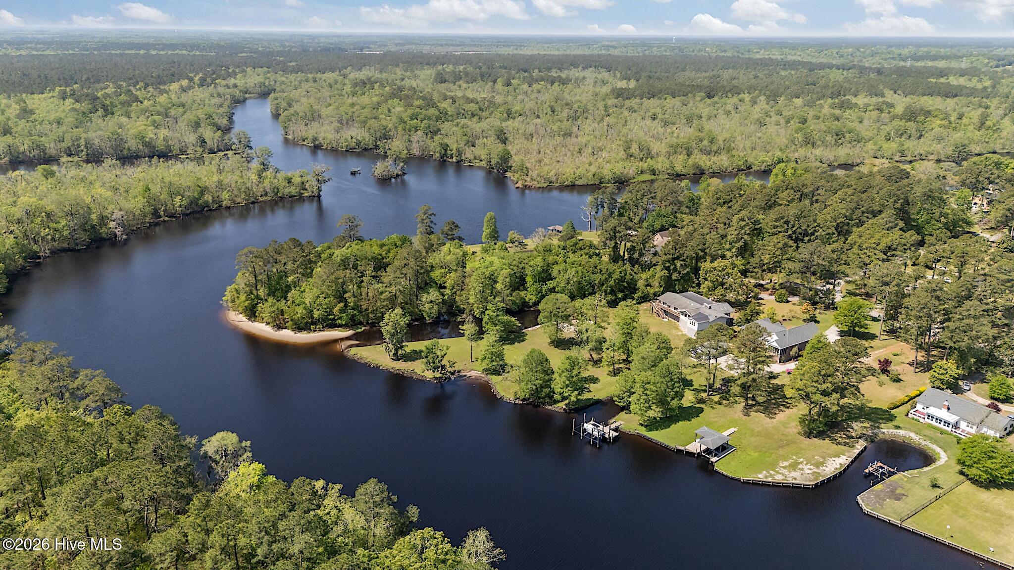 Aerial view of waterfront homes along a winding river, surrounded by dense woodland.