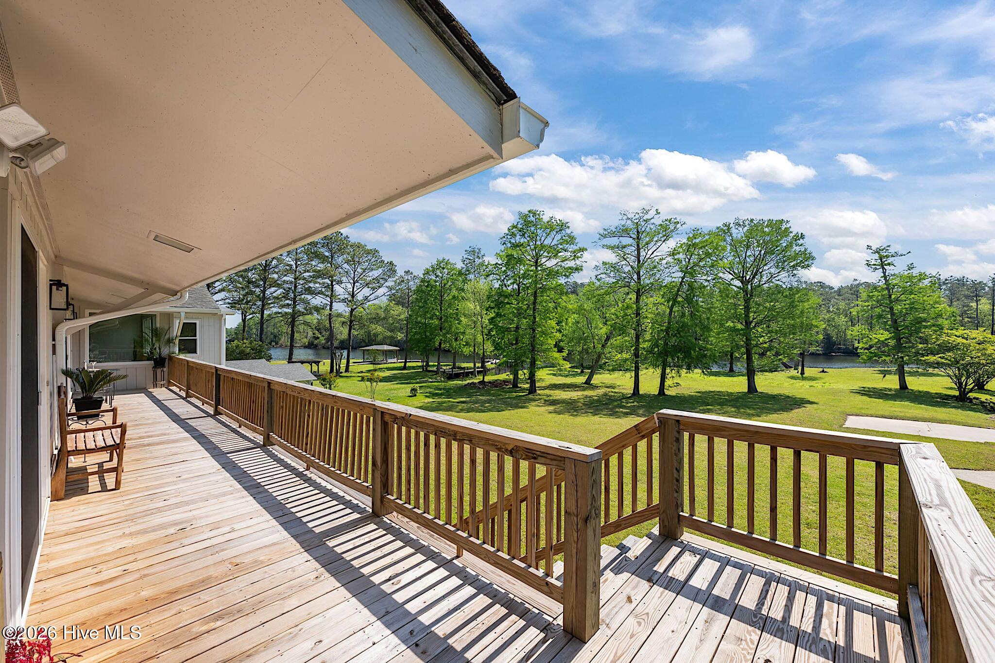 Wooden deck overlooking a tree-lined lawn and water, with a covered porch and outdoor seating.