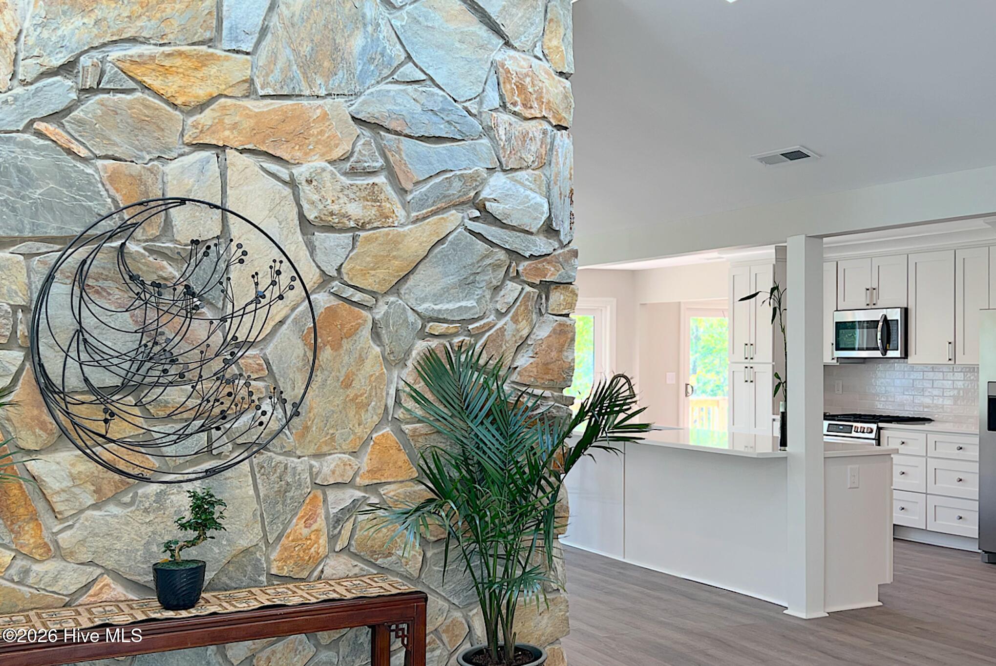 Open kitchen with white cabinetry and island beside a floor-to-ceiling stone accent wall.