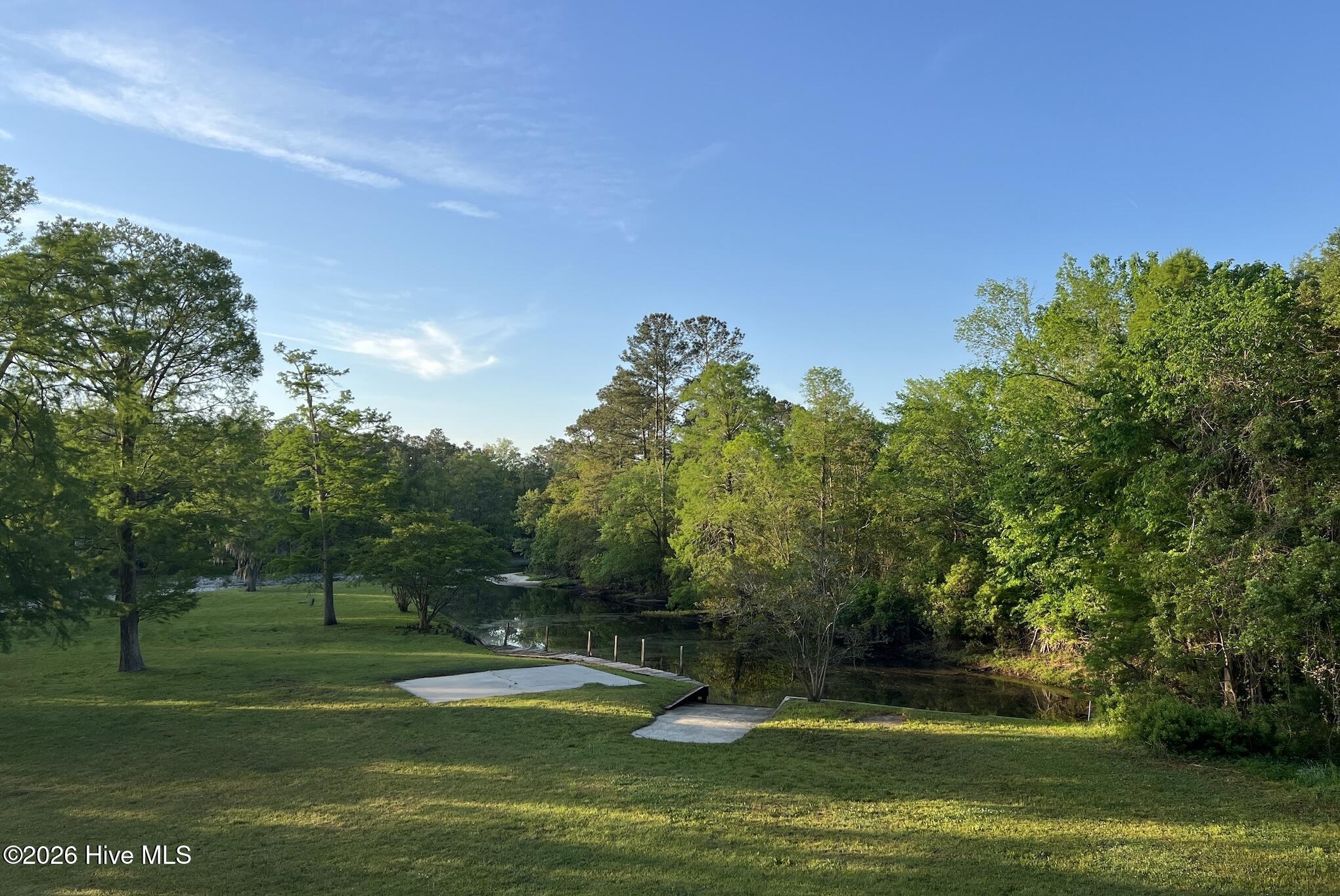 Waterfront yard with a wooded creek, grassy lawn, and concrete pads beside a small landing.