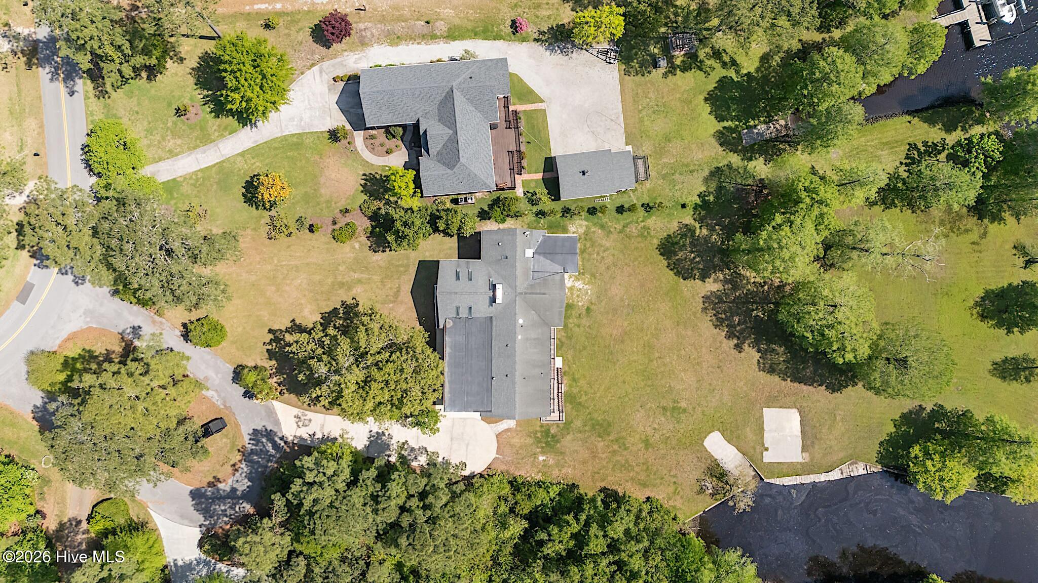 Aerial view of a gray-roofed home, detached outbuilding, landscaped grounds, and adjoining water.