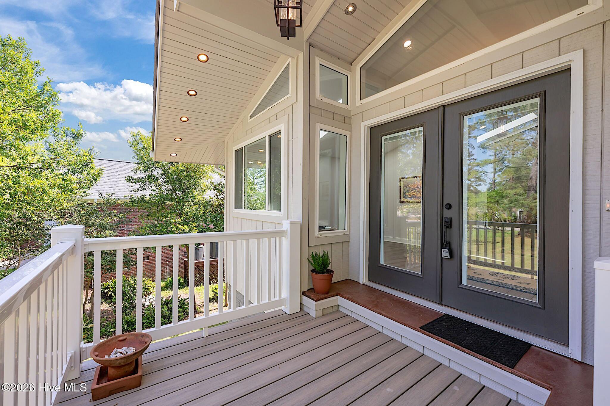 Covered front porch with gray double doors, white railings, and composite decking.
