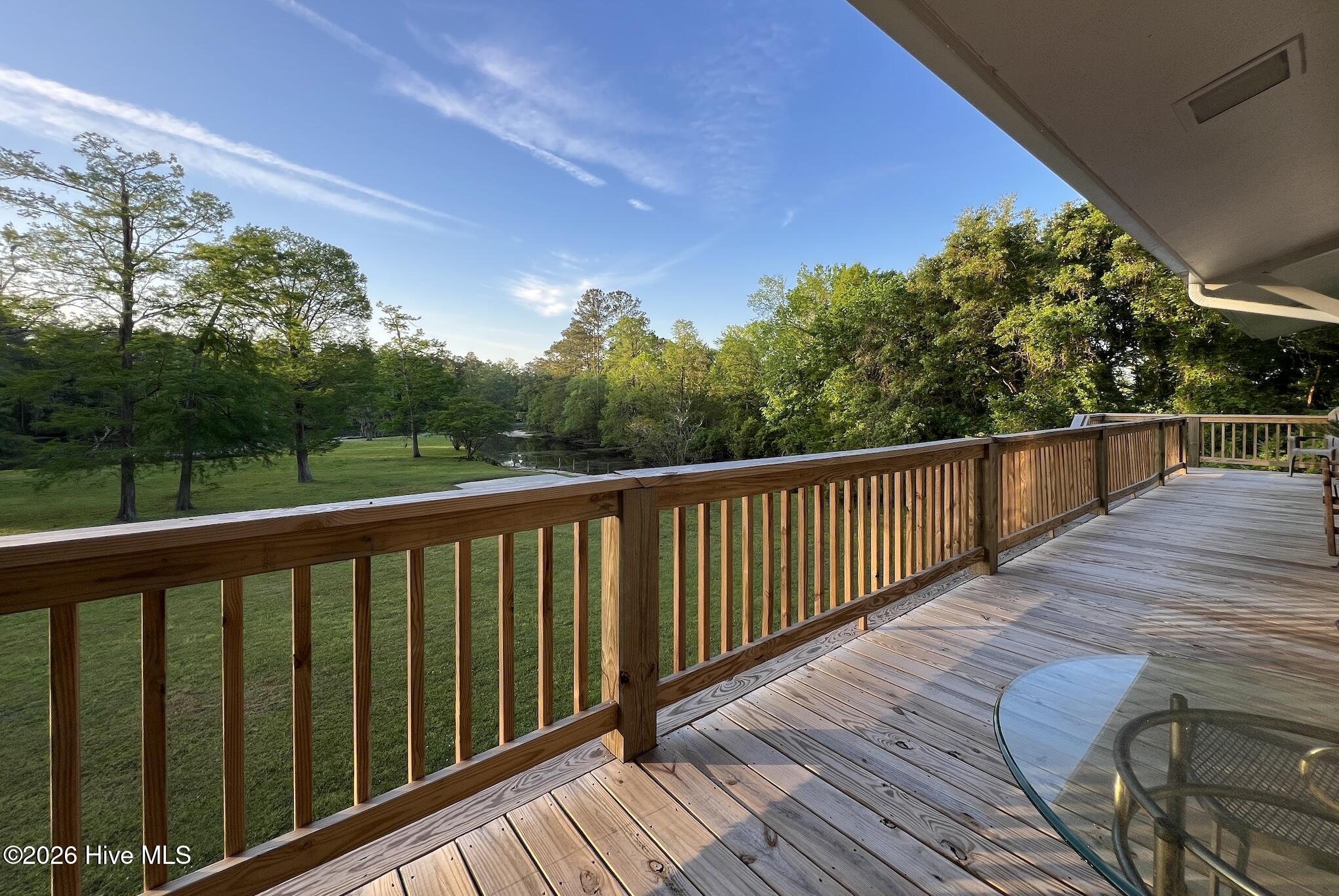 Wooden deck overlooking a tree-lined lawn and small creek, with a glass patio table.