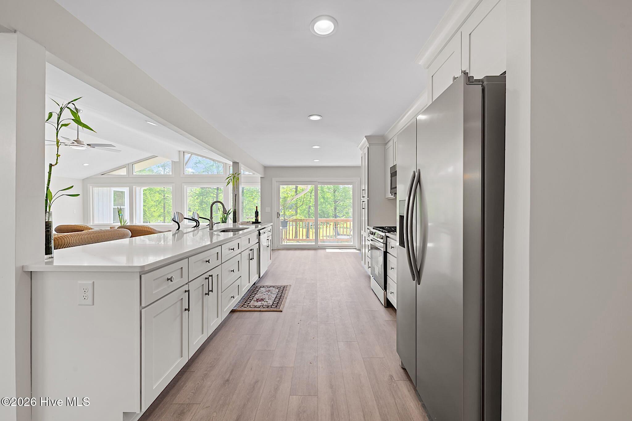 Bright white kitchen with a long island, stainless steel appliances, and sliding doors to a deck.