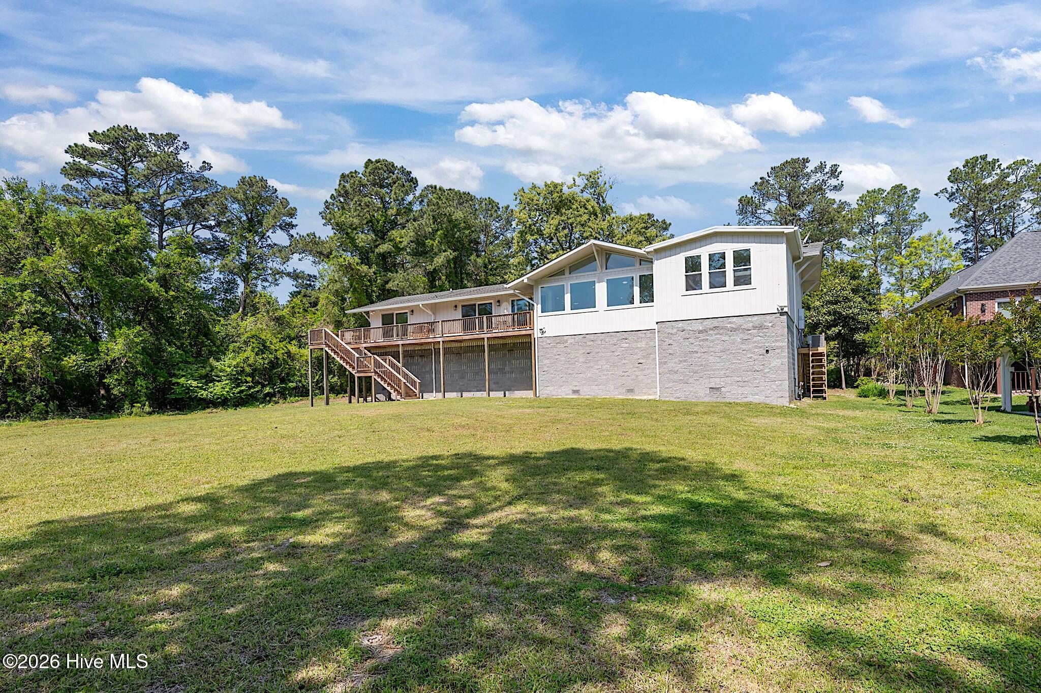 Raised white home with a long elevated deck and stairs overlooking a broad grassy yard.
