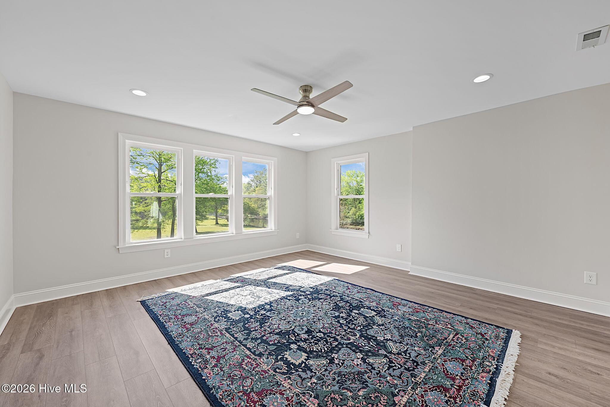 Bright empty room with multiple windows, a ceiling fan, and a large patterned rug.