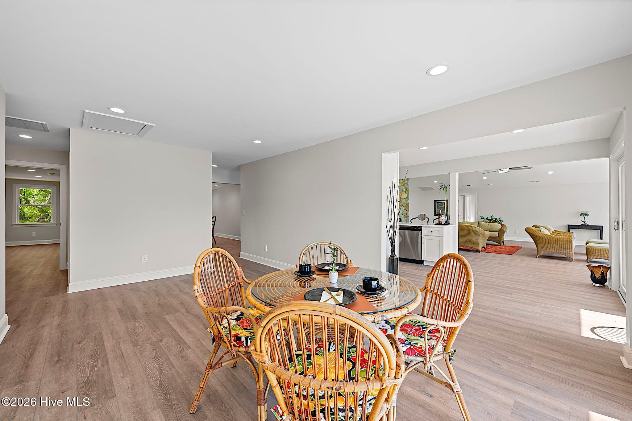 Dining area with a glass-top table and colorful wicker chairs, opening into a furnished living room.