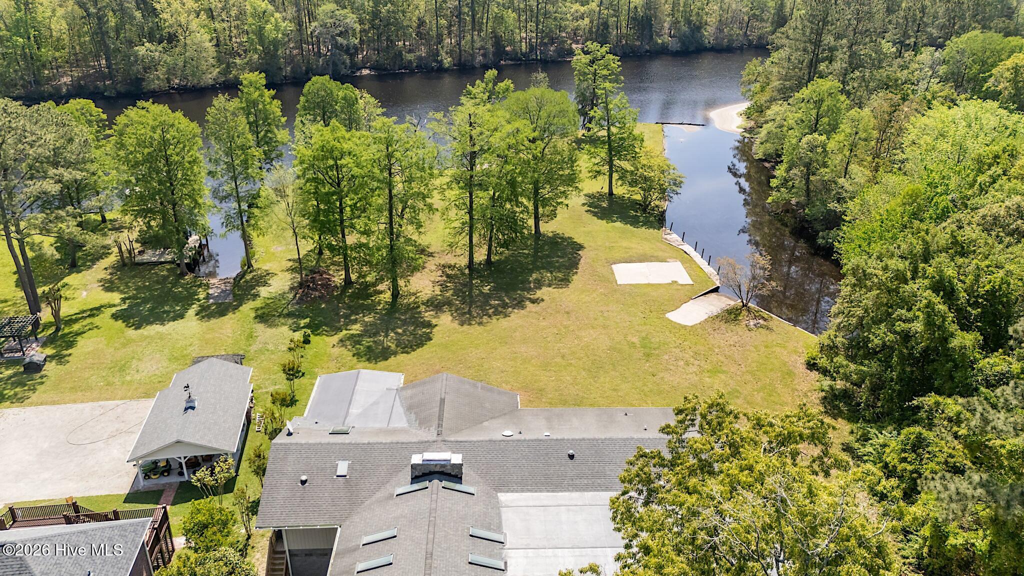 Aerial view of a wooded waterfront property with a broad lawn, dock, and sandy shoreline.