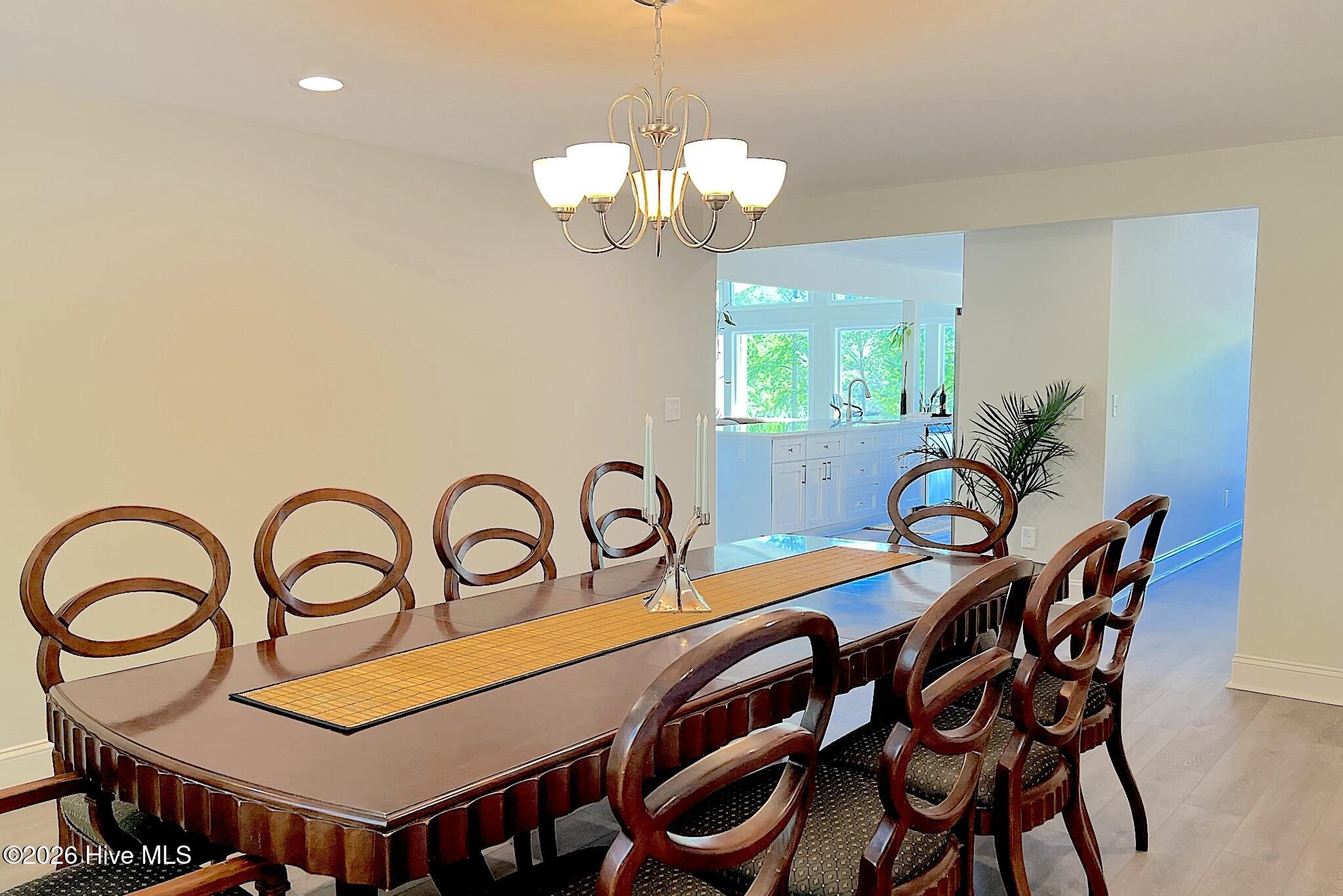 Dining room with a long wooden table and loop-back chairs beside a bright kitchen.