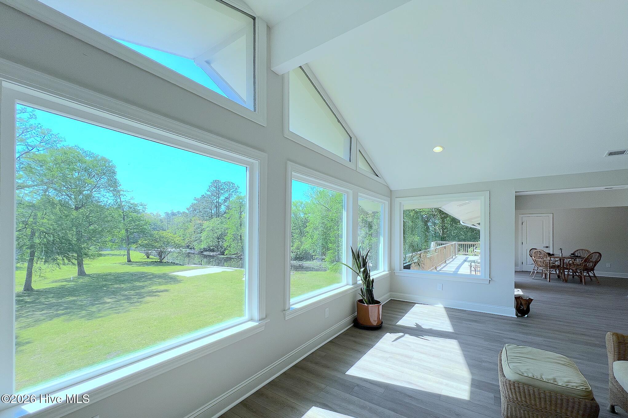 Bright vaulted living area with tall windows overlooking a tree-lined lawn and water.