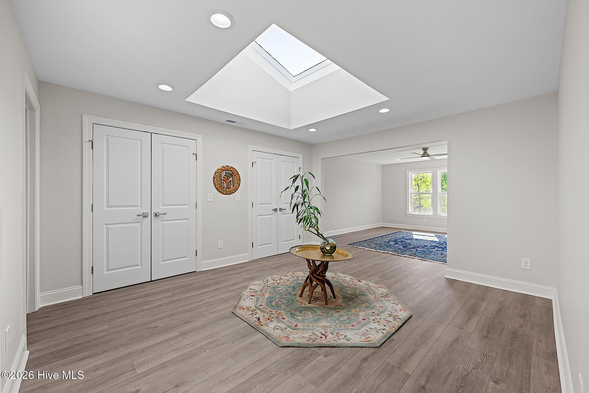 Bright entry area with a large skylight, white double doors, and a small table on a patterned rug.