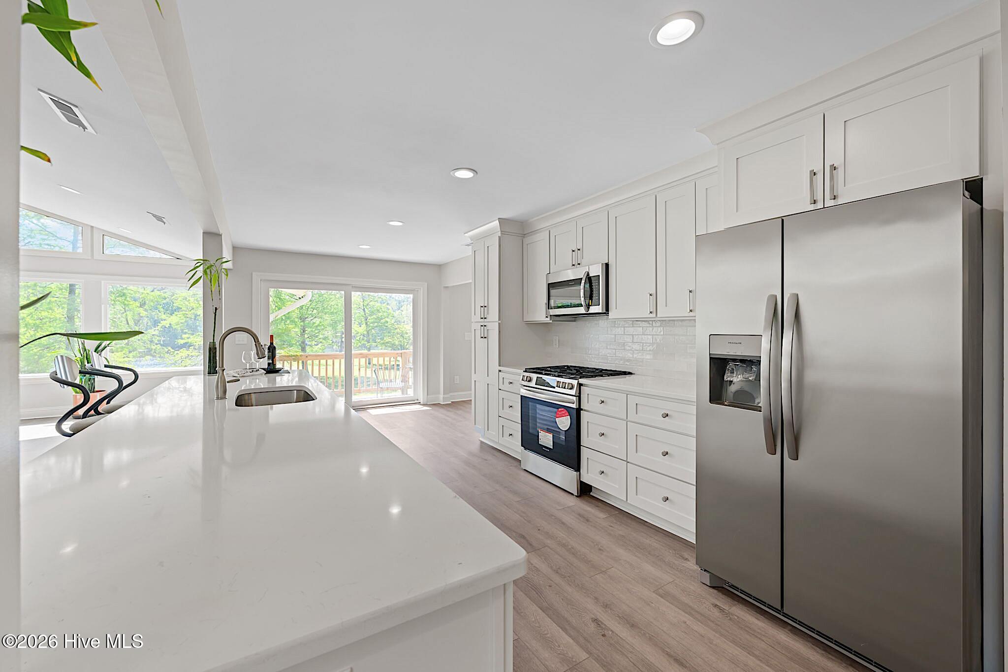 Bright white kitchen with a large quartz island, stainless steel appliances, and sliding glass doors to a deck.