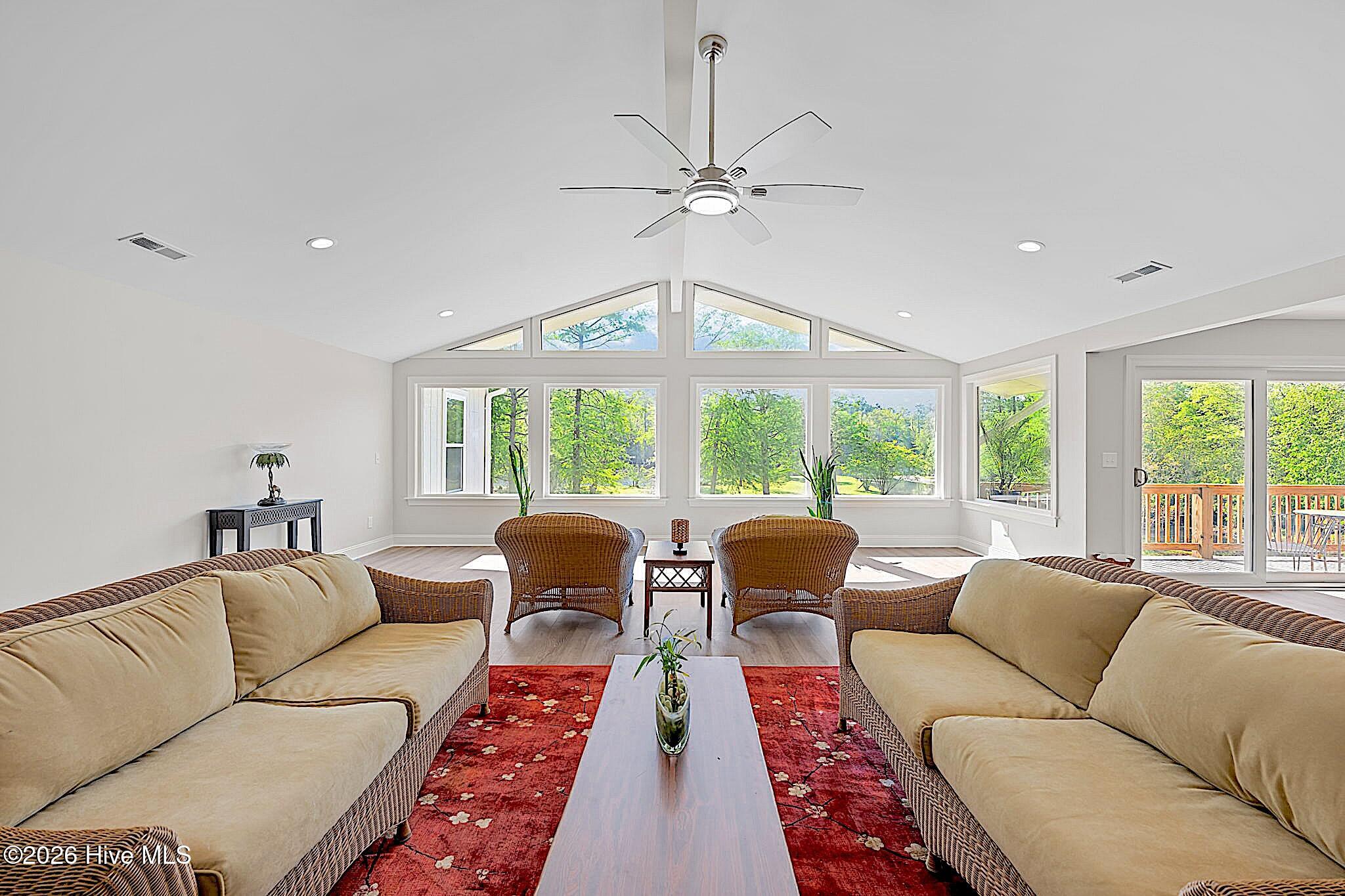 Living room with wicker seating, vaulted ceiling, large windows, and sliding doors to a deck.