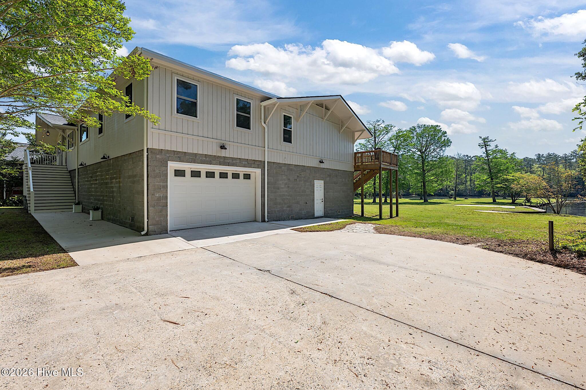 Two-story home with a large driveway, raised deck, and lawn beside the water.