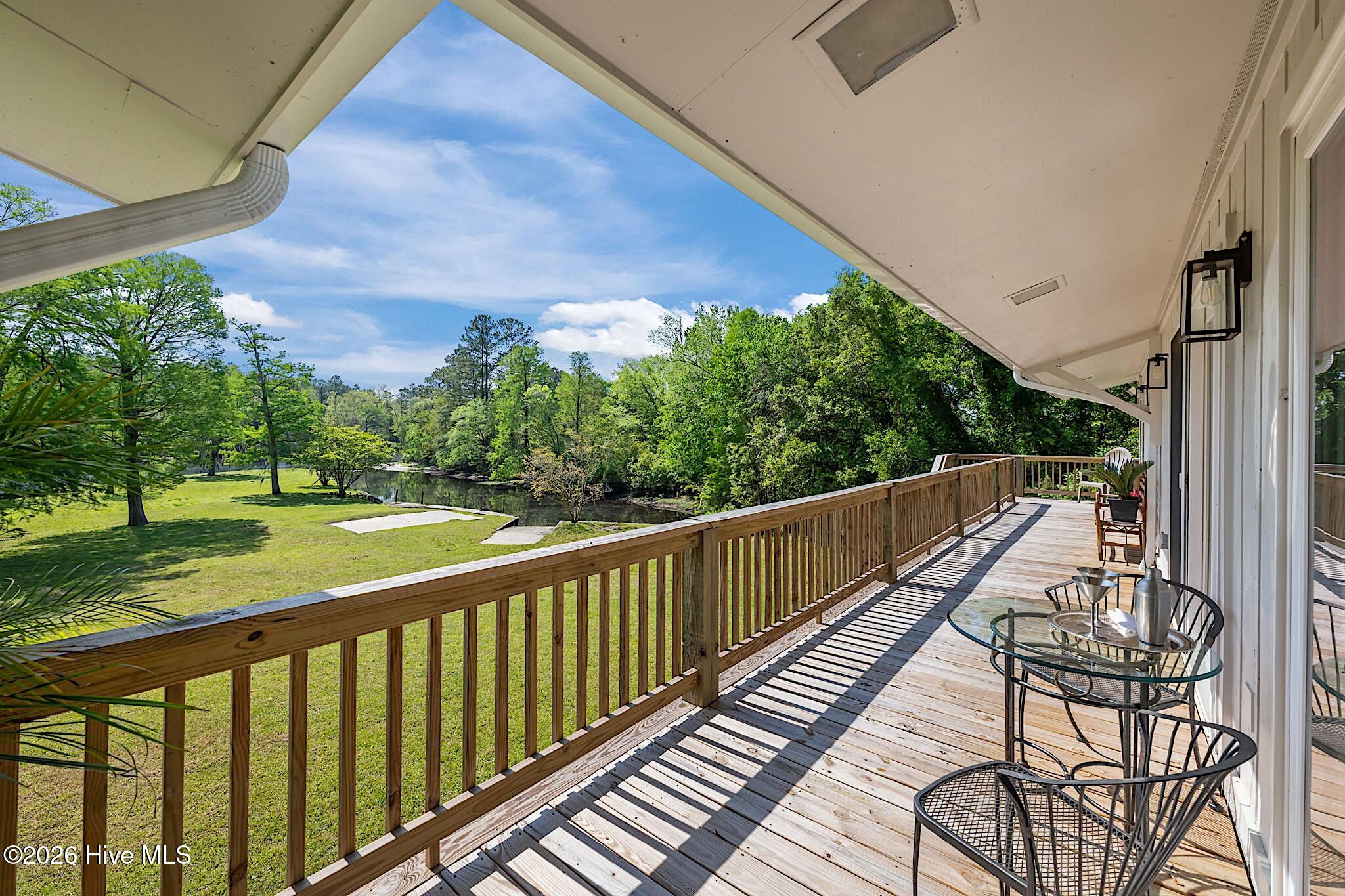 Wooden deck with outdoor seating overlooking a green lawn, water, and trees.