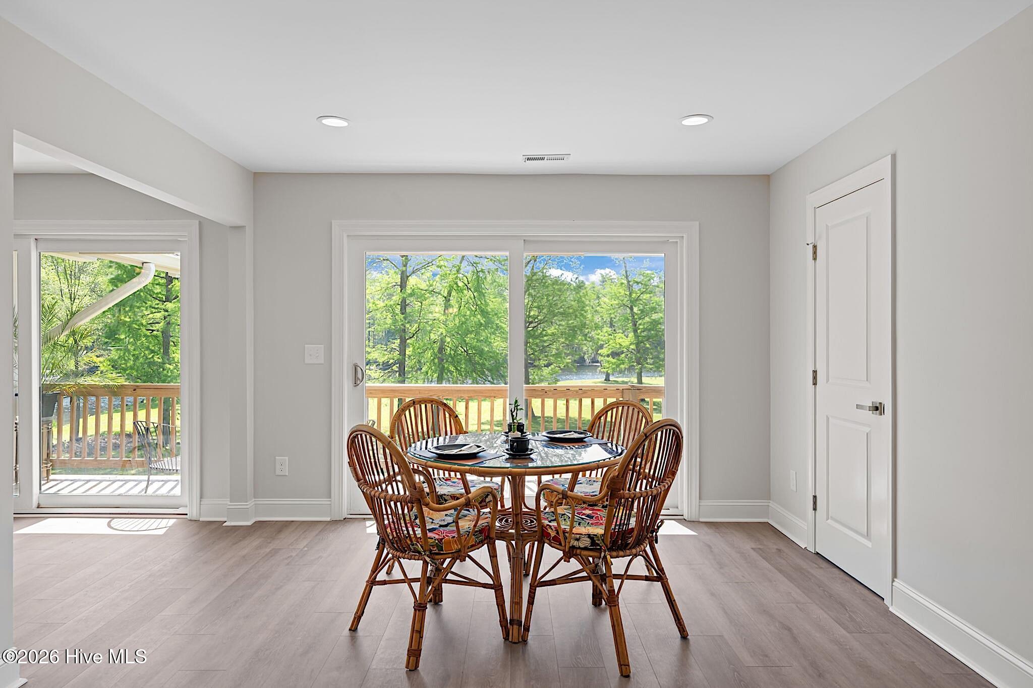 Dining area with a set table and wicker chairs overlooking a deck and water.