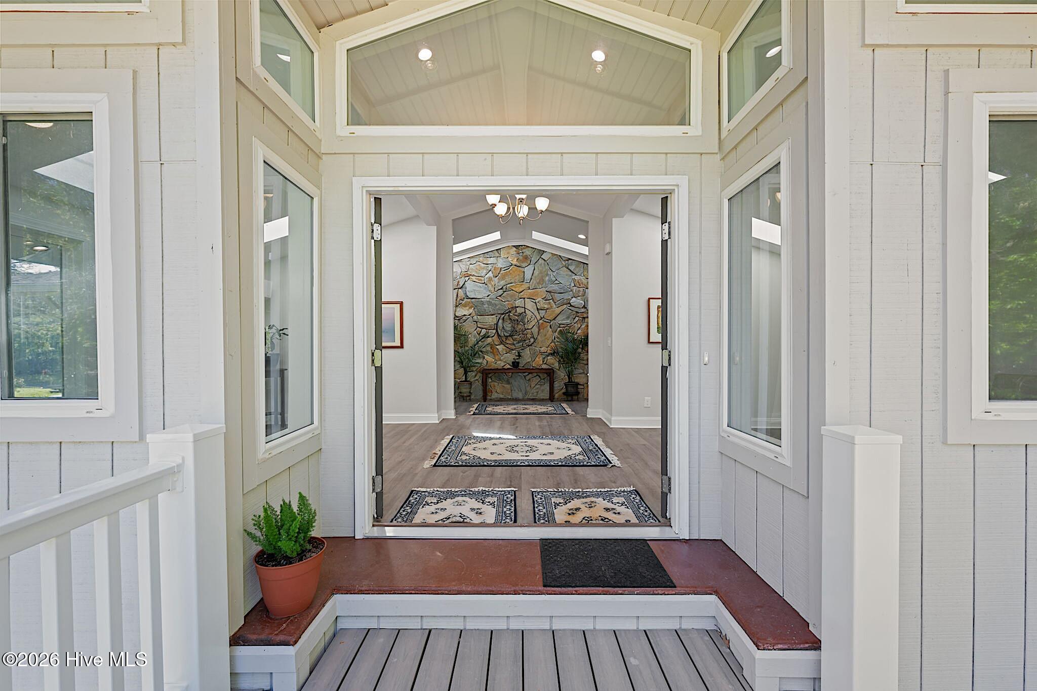 Front entry opens to a bright foyer with high windows, patterned rugs, and a stone fireplace wall.