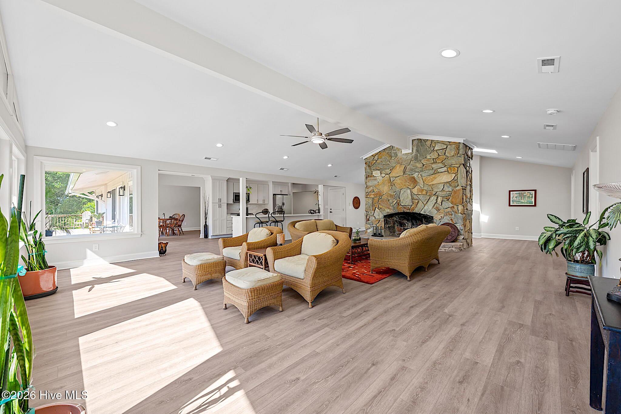 Living room with wicker seating, a tall stone fireplace, and a view into the open kitchen.