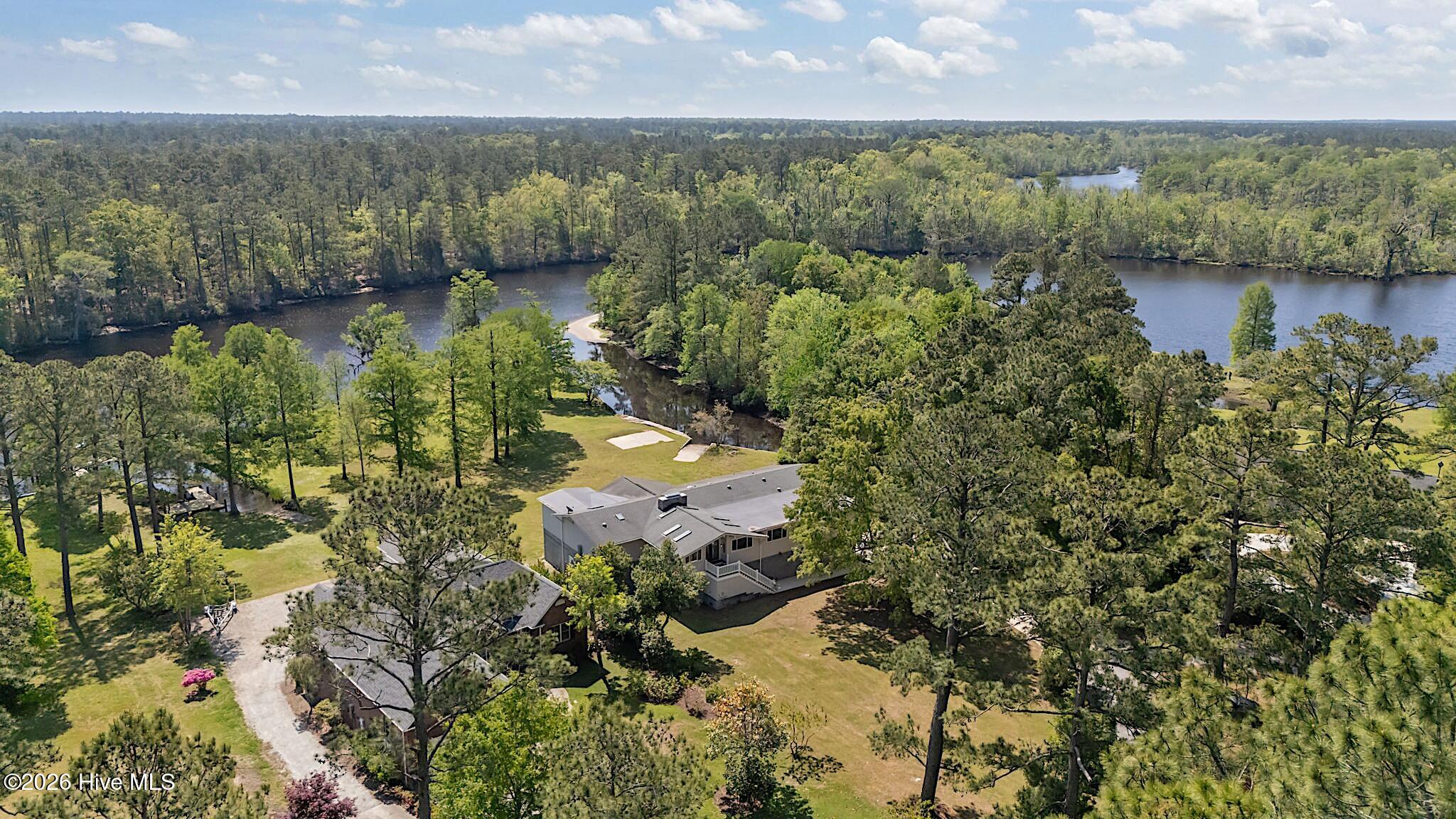 Aerial view of a home beside a winding river, surrounded by wooded grounds.