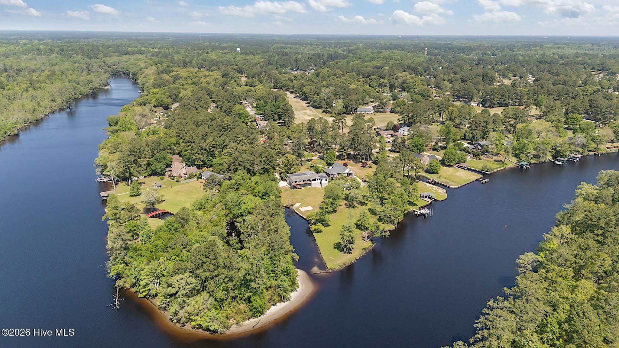 Aerial view of a wooded waterfront neighborhood with homes, docks, and a sandy point.