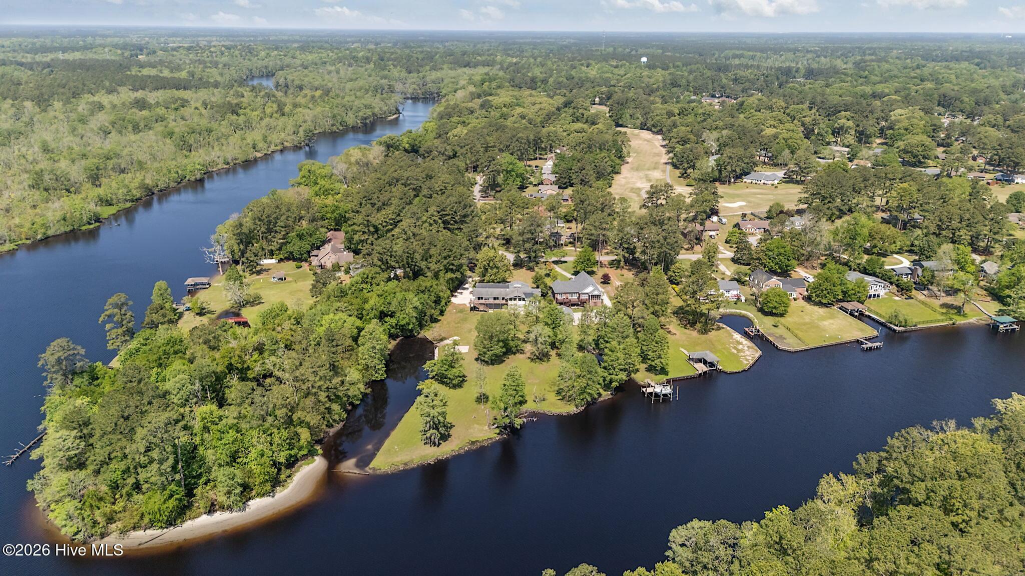 Aerial view of a wooded waterfront neighborhood with riverfront homes, docks, and a nearby golf course.