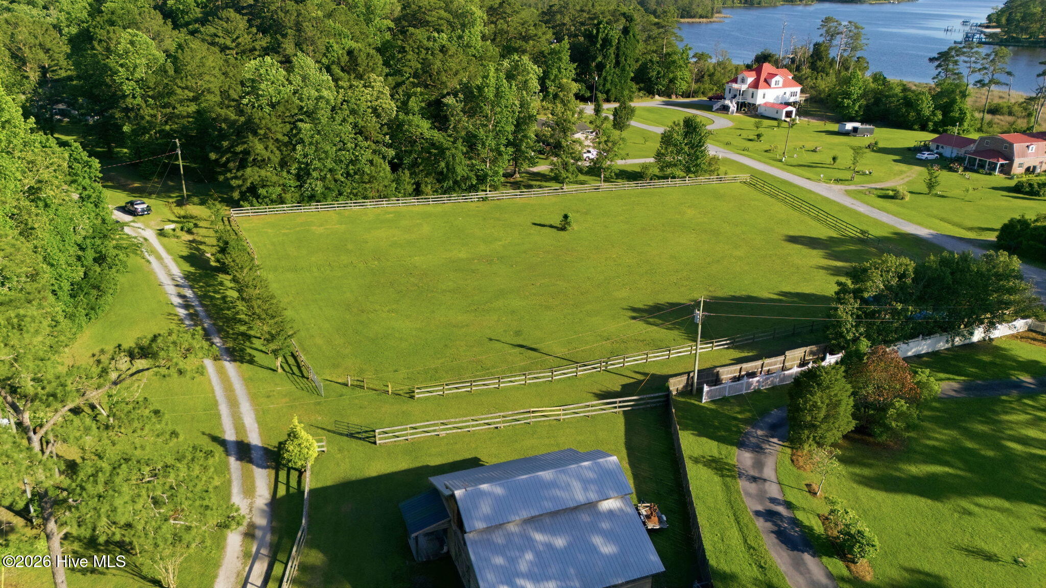 Aerial view of fenced grassy lots bordered by trees, with a waterway in the distance.