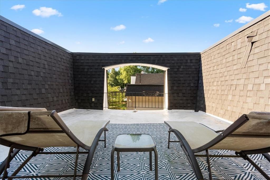Enclosed rooftop patio with lounge chairs, a patterned rug, and an arched opening to the greenery beyond.