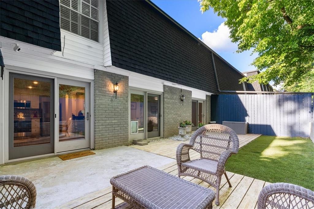 Home’s rear patio with sliding glass doors, woven seating, wooden deck, and enclosed lawn.