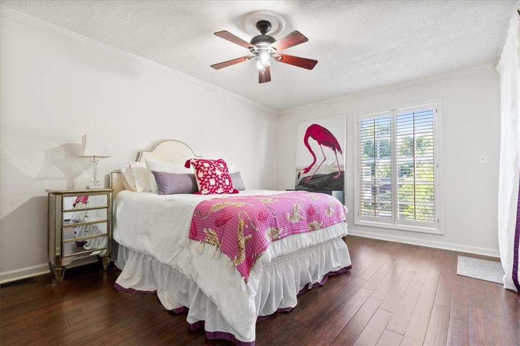 Bedroom with pink patterned bedding, dark hardwood floors, flamingo artwork, and plantation shutters.