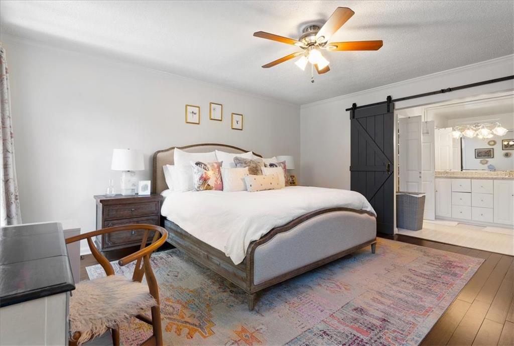 Furnished bedroom with a white bed, black sliding barn door, and adjoining bathroom vanity.