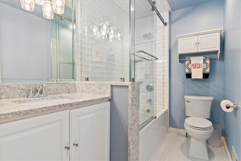 Bathroom with a glass shower, white vanity, speckled stone countertop, and pale blue walls.
